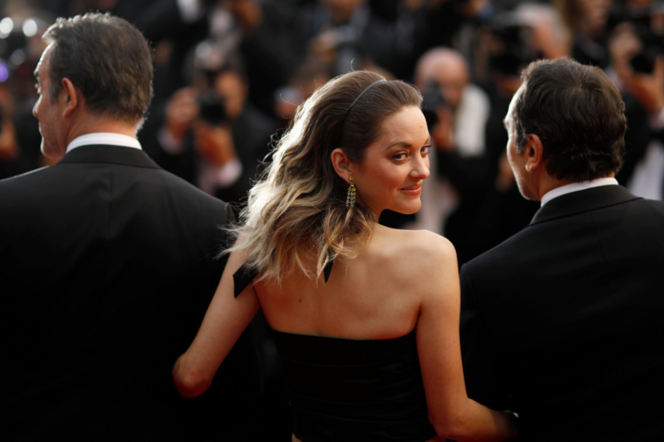 Was wird nur aus dem Kino? Ein Bild aus goldenen Zeiten: Marion Cotillard, Schauspielerin aus Frankreich, steht vor der Premiere des Films "La Belle Epoque" im Rahmen der 72. Internationalen Filmfestspiele eingehakt zwischen zwei Männern auf dem Roten Teppich.