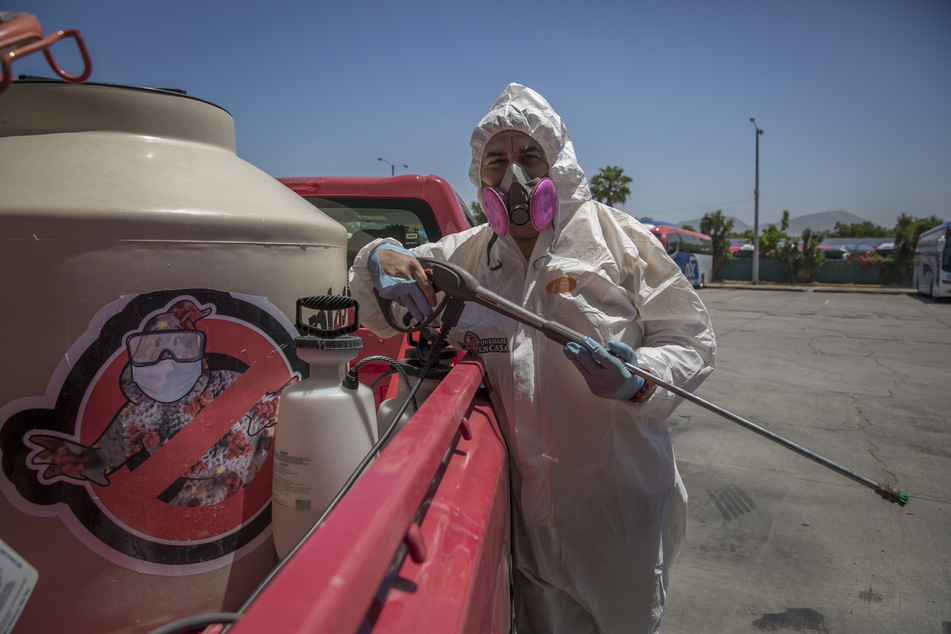 Ein Mitglied der Gruppe "Covid Busters" steht in Schutzanzug neben dem Wagen mit der Logo der Gruppe am Rande einer Desinfektionsaktion gegen die Ausbreitung des Covid-19.