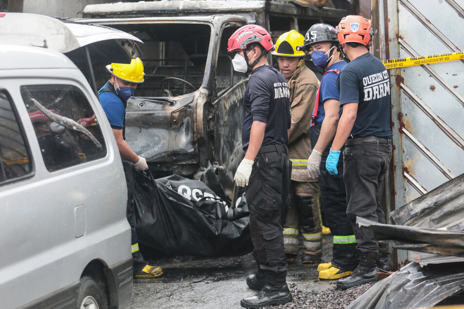 Feuerwehrleute tragen einen Leichensack mit den Überresten eines Opfers aus dem abgebrannten Gebäude.