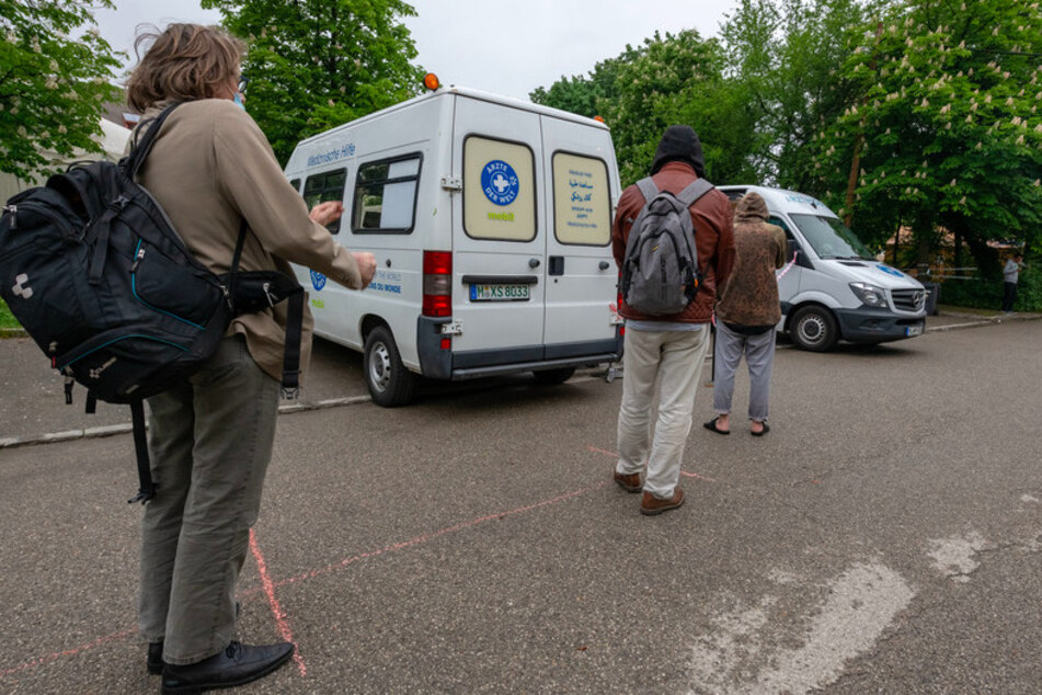 Männer warten mit Abstand vor zwei weißen Behandlungsbussen der Organisation "Ärzte der Welt" in München.