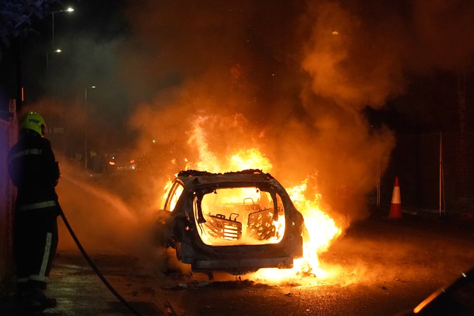 Feuerwehrleute kümmern sich um ein brennendes Polizeiauto, während Beamte nach einem gewalttätigen Protest in den Straßen von Hartlepool im Einsatz sind.