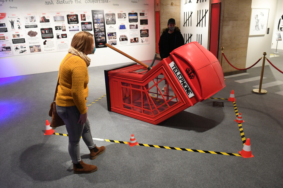 Besucher betrachten in der Ausstellung "The Mystery of Banksy – A Genius Mind" bei einem Presserundgang eine Reproduktion einer Arbeit des Künstlers Banksy mit dem Titel "Death of a Phonebooth".