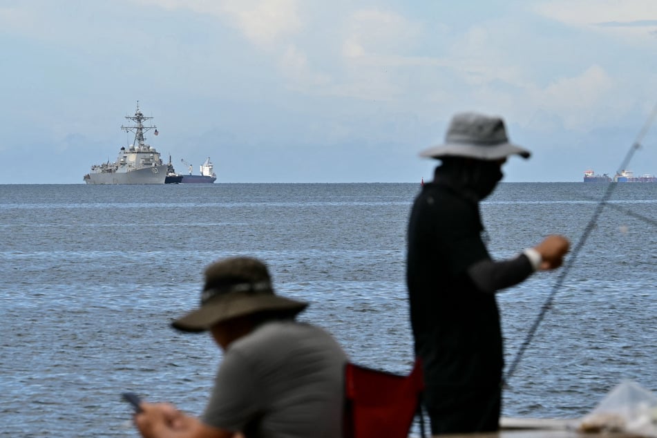 The USS Gravely warship is seen at a distance off the coast of Port of Spain on October 26, 2025, as fishermen fish in the Trinidadian capital.