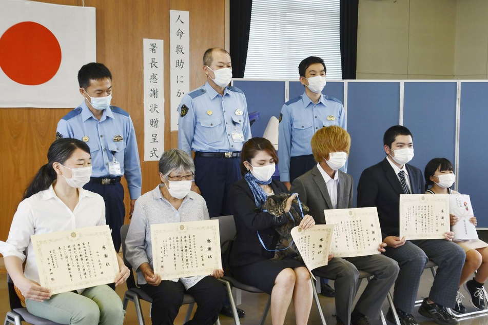 Tomoko Nitta (vorne, M) sitzt mit ihrem Kater Koko in der Polizeistation zwischen ihren Nachbarn. Auch diese hatten Dankesurkunden aufgrund der Rettung erhalten.