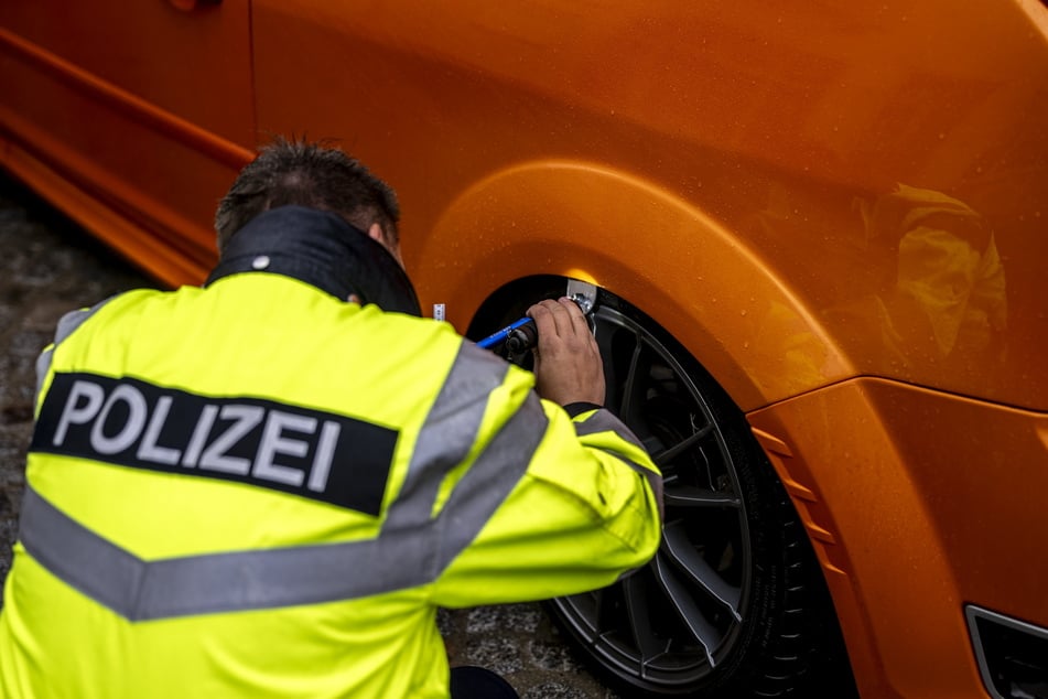 Ein Polizeibeamter kontrolliert den Radkasten eines tiefergelegten Fords.