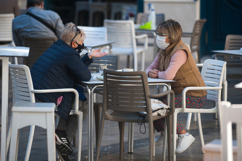 Zwei Frauen mit Mund-Nasen-Schutz sitzen im Außenbereich einer Bar in Malaga.