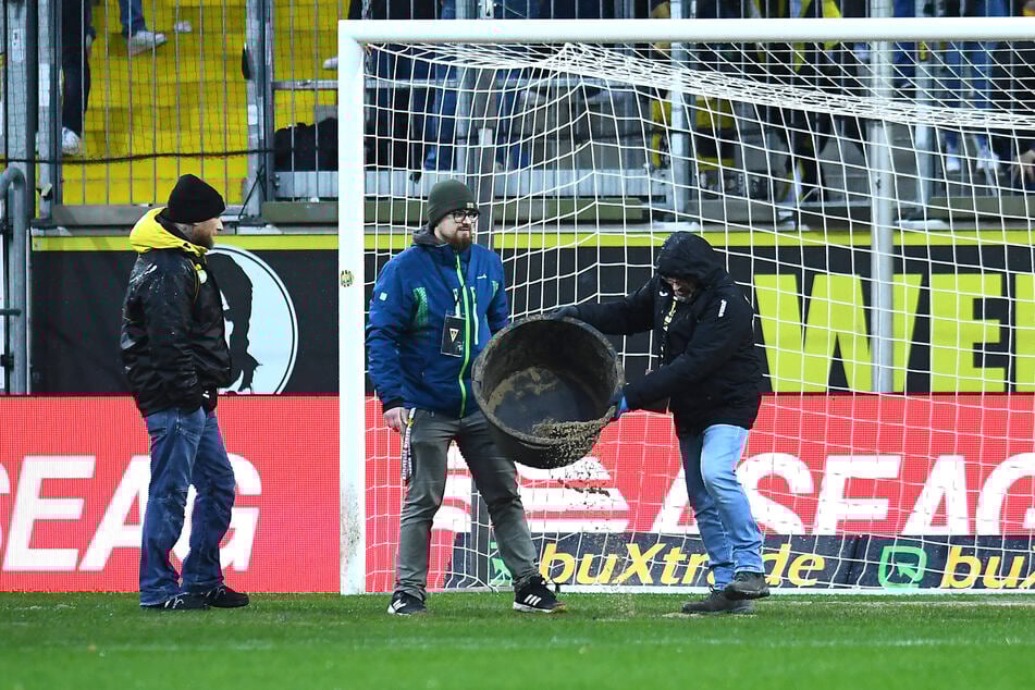 Dauerregen stellt den Platz teilweise unter Wasser, Aachen-Mitarbeiter bessern einen Strafraum mit Sand aus.