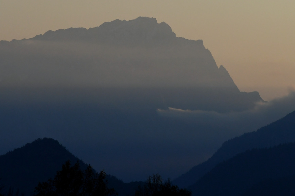 Nebel zieht während des Sonnenuntergangs im Wettersteingebirge herein, in der Mitte ist die Zugspitze zu sehen.