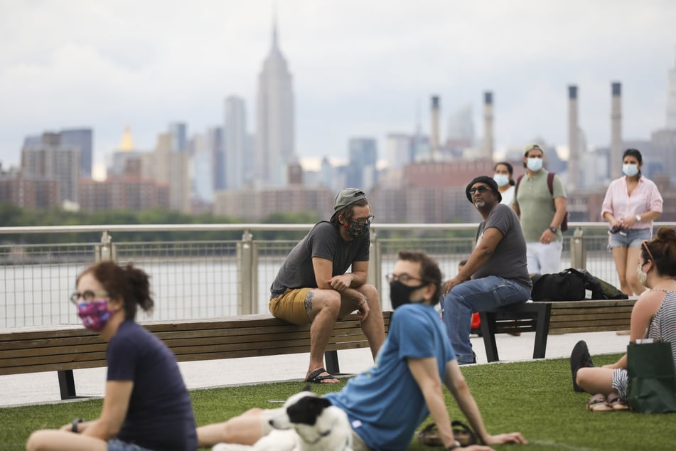 Menschen, die zum Schutz vor der Verbreitung des Coronavirus Mundschutze tragen, sitzen im "Domino Park" am Fluss "East River".