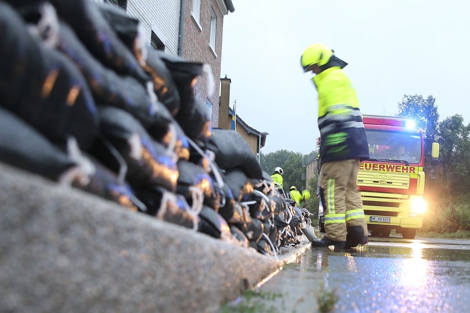 Feuerwehrleute errichten am Erkrather Straßenrand eine Wassersperre aus Sandsäcken.
