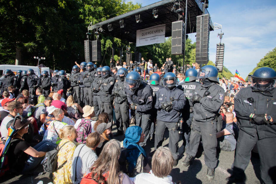 Polizisten stehen bei einer Kundgebung gegen die Corona-Beschränkungen auf der Straße des 17. Juni zwischen Teilnehmern vor einer Bühne.