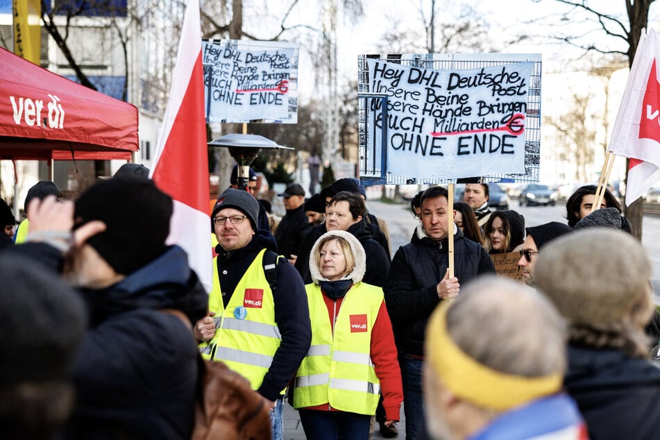 "Hey, DHL, Deutsche Post - Unsere Beine, unsere Hände bringen euch Millionen ohne Ende" steht auf dem Banner bei einer Kundgebung vor einem Briefzentrum in München am Montag.