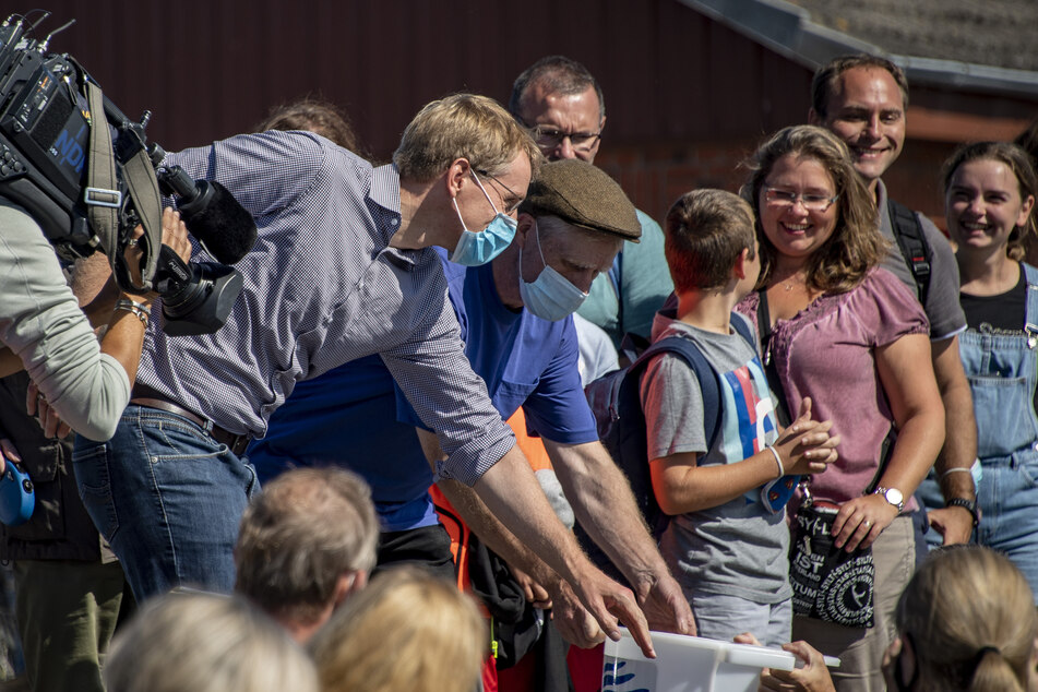 Daniel Günther (47, l.), Ministerpräsident von Schleswig-Holstein, hilft Gefäße mit Jungaalen in ein Boot zu tragen.