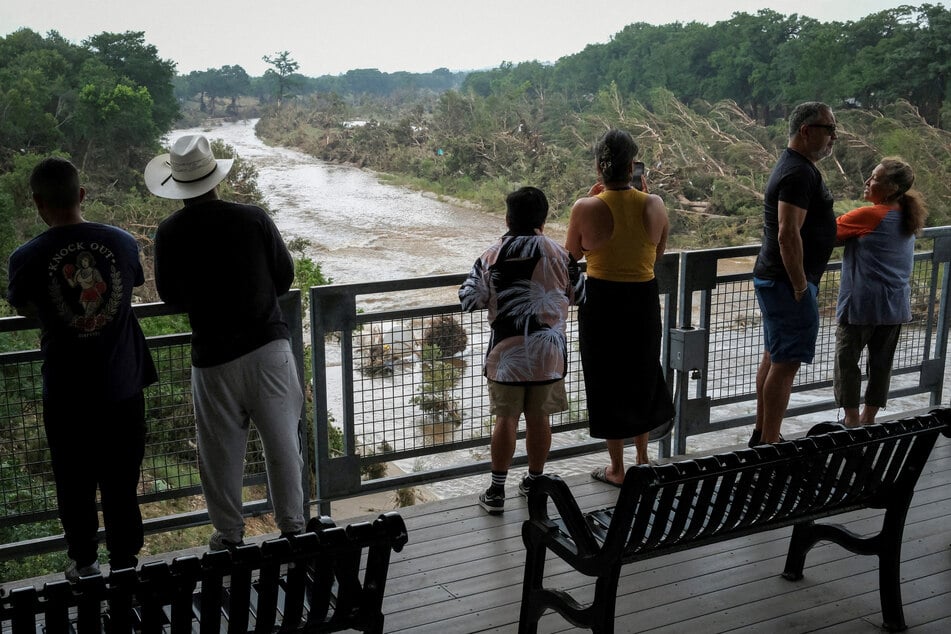People look out at the Guadalupe River following flash flooding, as they gather after receiving an SMS alert on potential floods in the area, in Kerrville, Texas, on July 6, 2025.