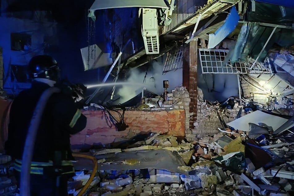 This handout photograph taken and released by the Ukrainian Emergency Service on Thursday, shows a rescuer working with a water hose to extinguish a fire at the site of a missile strike in Zaporizhzhia.