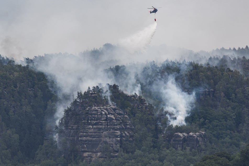 Ein Hubschrauber der Bundespolizei fliegt mit einem Löschwasser-Außenlastbehälter, um den Waldbrand zu löschen.