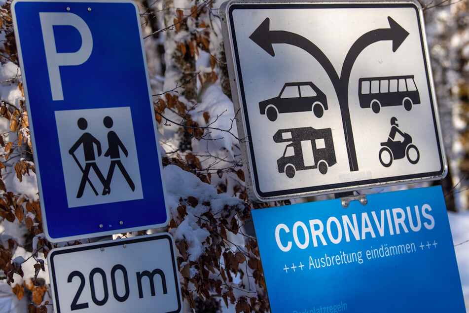 Ein verschneites Schild mit der Aufschrift "Coronavirus - Ausbreitung eindämmen" steht am Parkplatz von Schloss Linderhof.