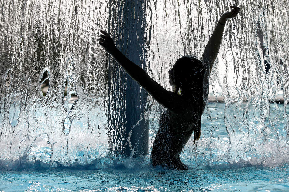 Eine Frau steht im Freibad unter einem Wasserpilz und erfrischt sich. (Symbolbild)