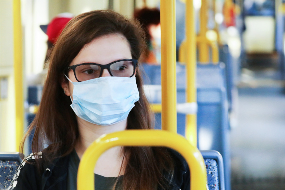 Eine Frau sitzt mit einer Maske in einer Tram.