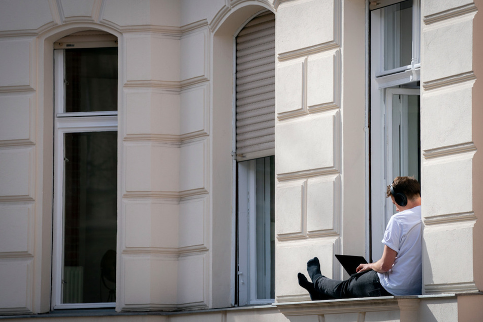 Ein Mann hat sein Homeoffice auf die sonnige Fensterbank seiner Wohnung verlegt.