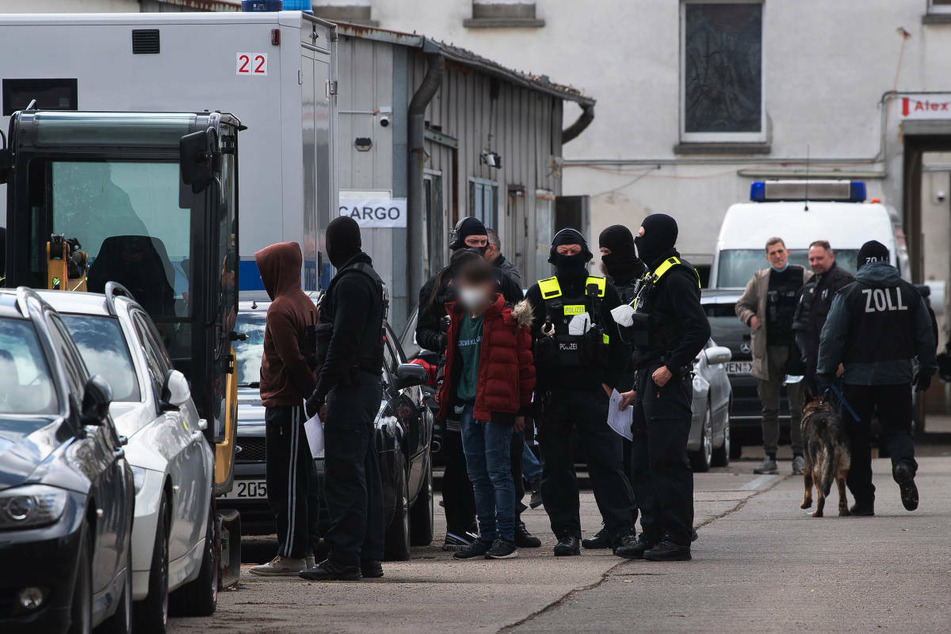 Einsatzkräfte der Polizei stehen im Rahmen einer groß angelegten Drogen-Razzia auf einem Gelände in Lichtenberg neben festgenommenen Personen.