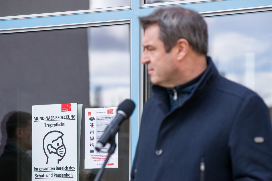 "Mund-Nase-Bedeckung Tragepflicht" steht auf einem Plakat am Sigena-Gymnasium neben Markus Söder (CSU), Ministerpräsident von Bayern, der nach dem Besuch einer Teststation für Corona-Schnelltests in der Schule zu Journalisten spricht.
