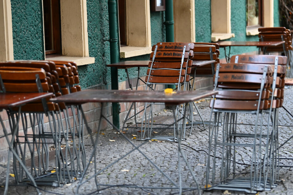 Stühle und Tische stehen zusammengestellt vor einem geschlossenen Restaurant.