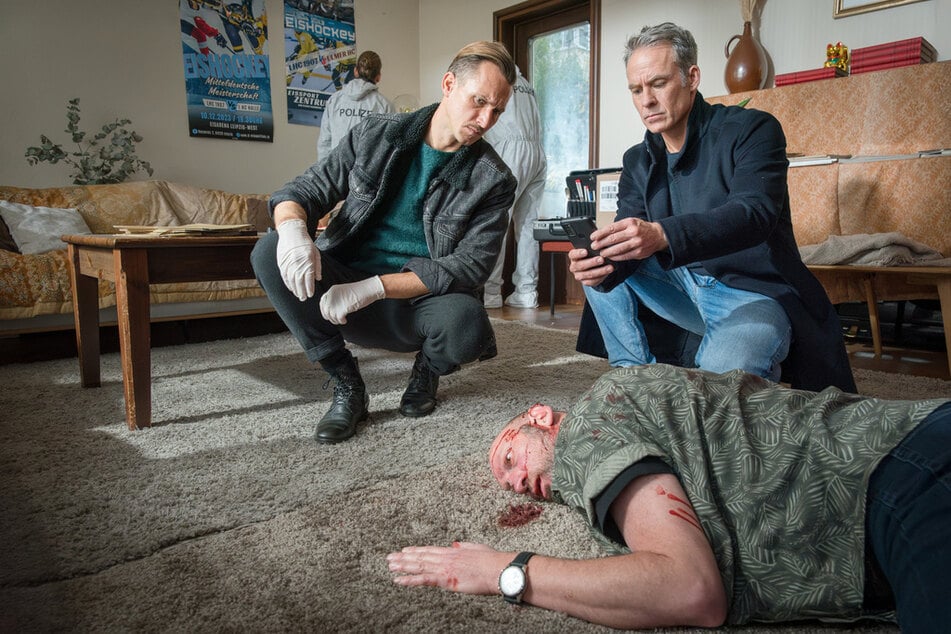 Moritz Brenner (Johannes Hendrik Langer, 40, l.) und Jan Maybach (Marco Girnth,55, r.) untersuchen den Tatort, an dem das Opfer Juri Kabowski (Volker Wackermann, M.)