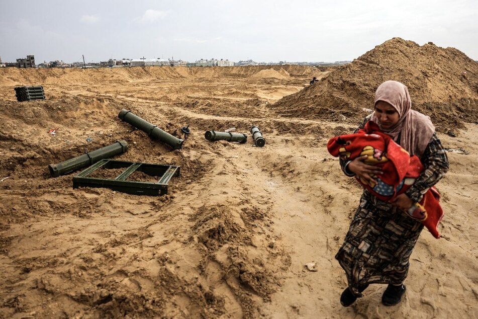 A Palestinian woman holding a baby walks past ammunition containers left behind by Israeli troops as she flees Khan Younis in the southern Gaza Strip.