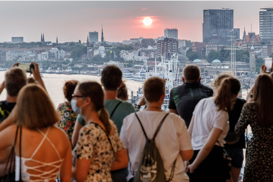 Besucher der Plaza der Elbphilharmonie betrachten den Sonnenuntergang im Westen Hamburgs.