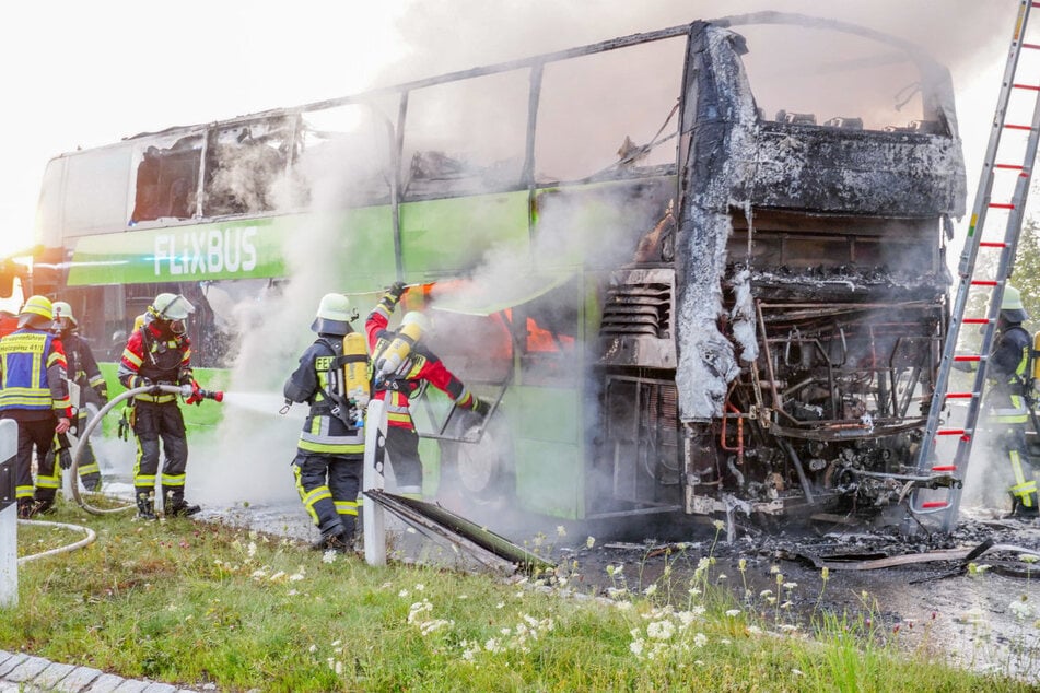 Feuerwehrleute löschen den Brand im Reisebus. Das Fahrzeug brennt vollständig aus.