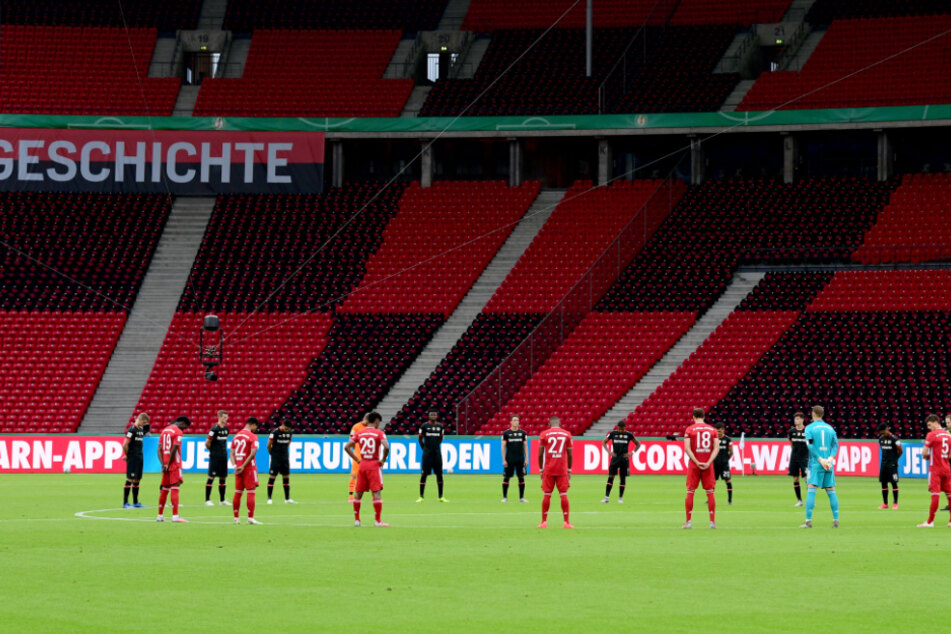 Vor menschenleeren Rängen halten die Spieler vor Anpfiff eine Schweigeminute für die Opfer der Corona-Pandemie ab.