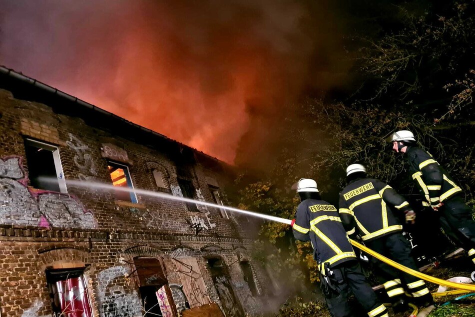 Feuerwehrleute löschen den Brand durch eines der kaputten Fenster. Das Dach steht dabei immer noch in Flammen, wie man an dem Feuerschein erkennen kann.