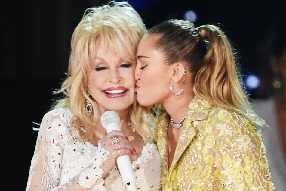 Miley Cyrus (r.) said that her godmother Dolly Parton (l.) is "excited" to get back to work after suffering complications from a kidney stone.