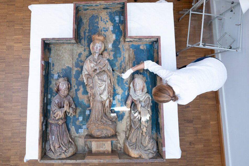 Eine Restauratorin arbeitet im Landesamt für Denkmalpflege in Dresden mit einem Staubpinsel an einem Schrein mit Altarfiguren aus der ehemaligen Wallfahrtskirche "Unserer lieben Frauen".