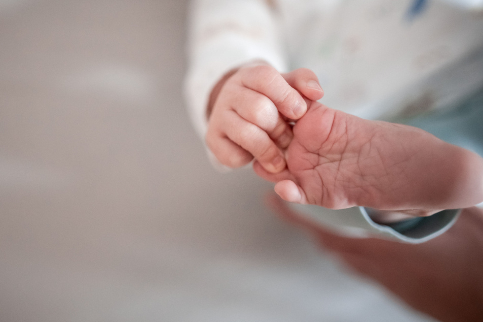 Ein Baby greift mit den Fingern nach seinem Fuß. (Symbolbild)