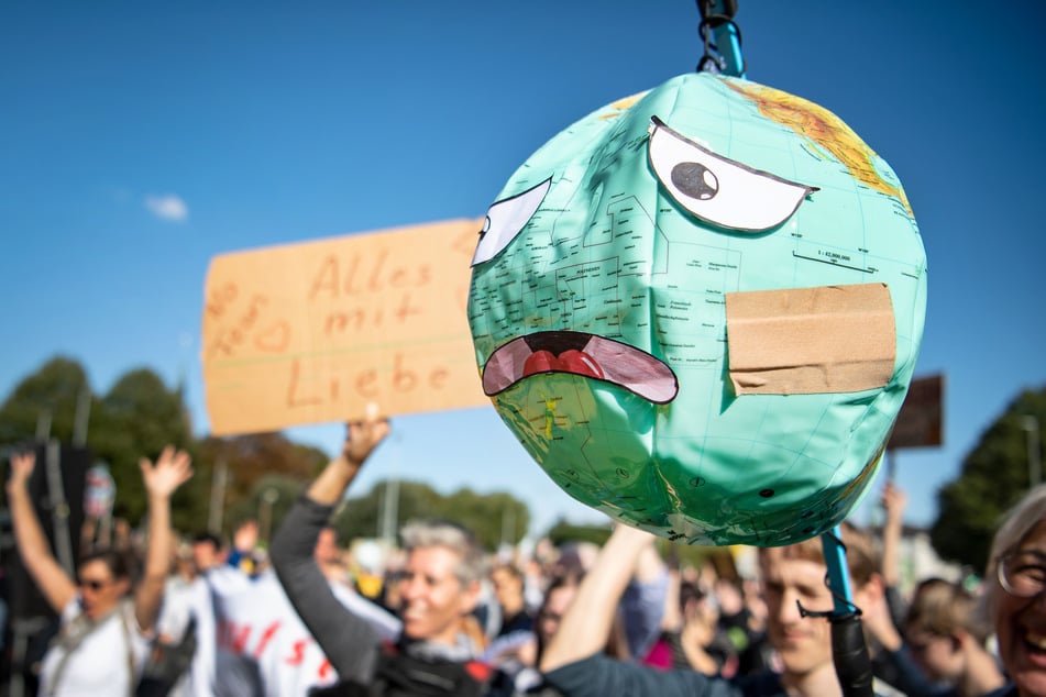 Demonstranten halten einen Luftballon mit Globusaufdruck hoch, der mit einem Pflaster und unglücklichen Gesichtszügen beklebt ist.