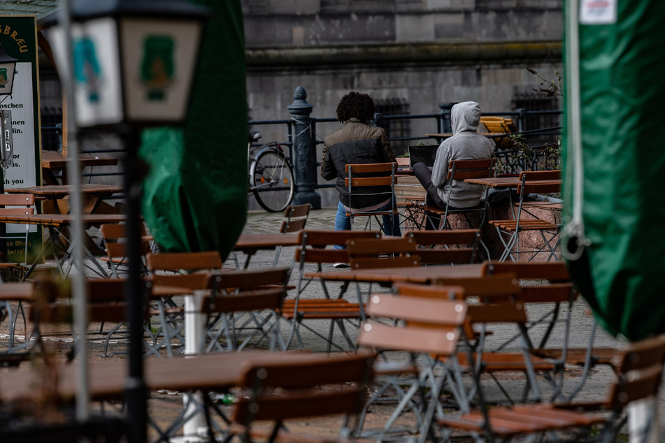 Zwei Männer sitzen auf Stühlen einer geschlossenen Außengastronomie im Nikolaiviertel.
