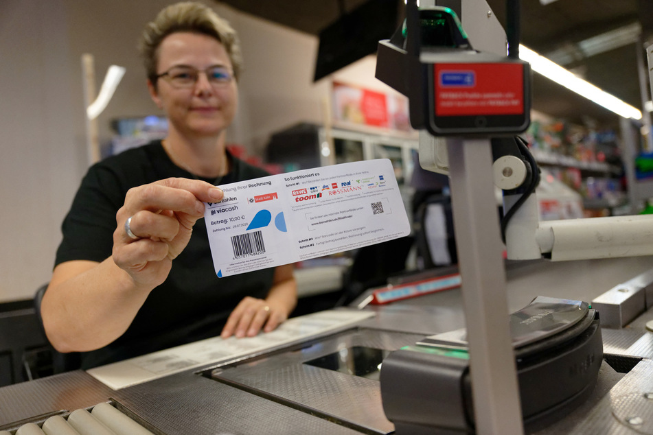Eine Mitarbeiterin in einer Rewe-Filiale hält ein Blatt mit einem Barcode bereit. In Köln können Knöllchen seit einem Jahr auch in Geschäften bezahlt werden.