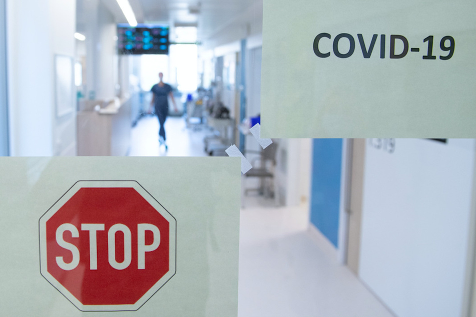 Eine Frau geht auf der Corona-Intensivstation hinter einer Glastür einen Gang entlang.