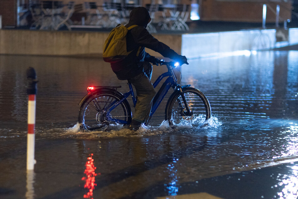 In Wismar muss ein Radfahrer durch das Hochwasser am Stadthafen fahren.