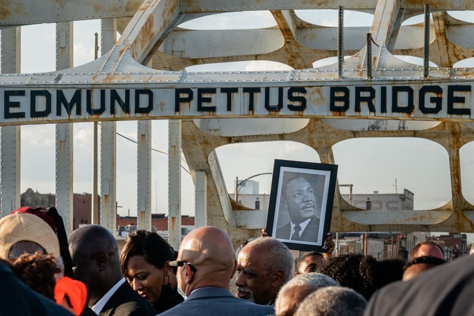 A man holds up a photo of the late Rev. Dr. Martin Luther King Jr. while marching across the Edmund Pettus Bridge in Selma, Alabama.