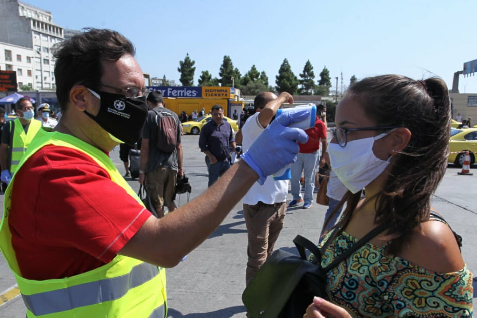 A medical employee wearing a protective mask measures the body temperature of passengers on a ferry at the port.