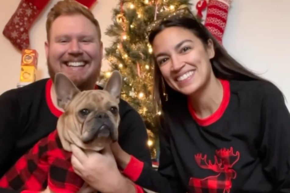 AOC, her fiancé Riley Roberts, and their dog Deco pose in matching holiday PJs.