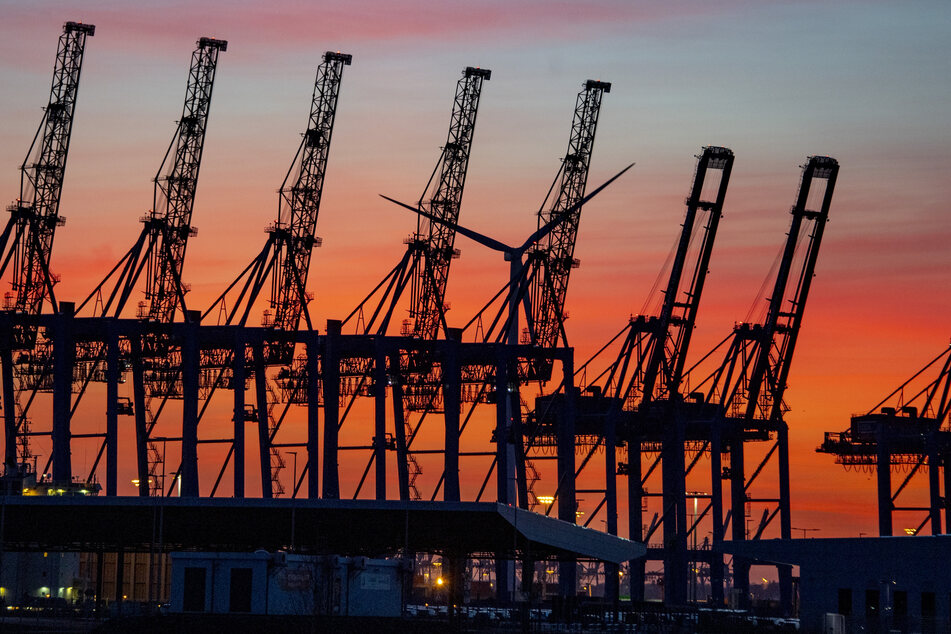 Die Sonne geht hinter den hochgeklappten Containerbrückenkränen, die normalerweise Schiffe entladen, im Hamburger Hafen unter. (Symbolfoto)