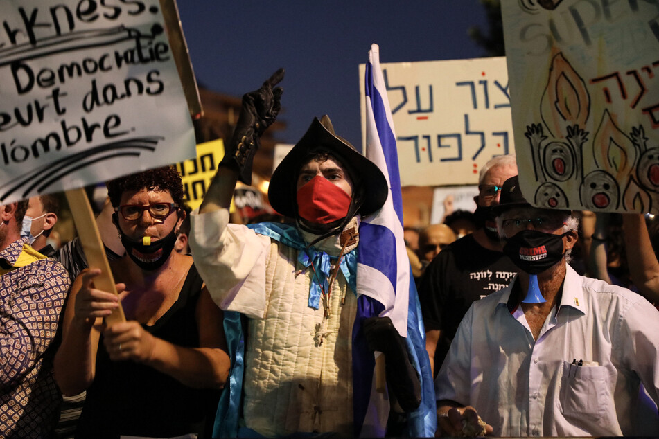 Demonstranten halten Plakate und Fahnen bei einem Protest gegen den israelischen Premierminister Netanjahu in der Nähe seiner Residenz in die Höhe.