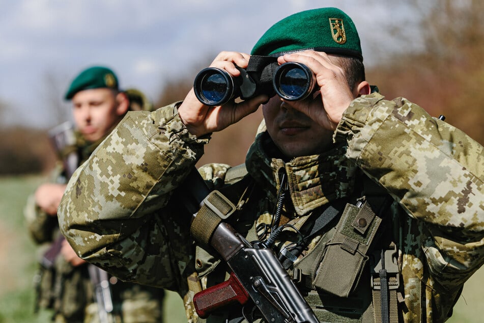 Ein ukrainischer Grenzschützer sucht mit einem Fernglas die Umgebung ab.