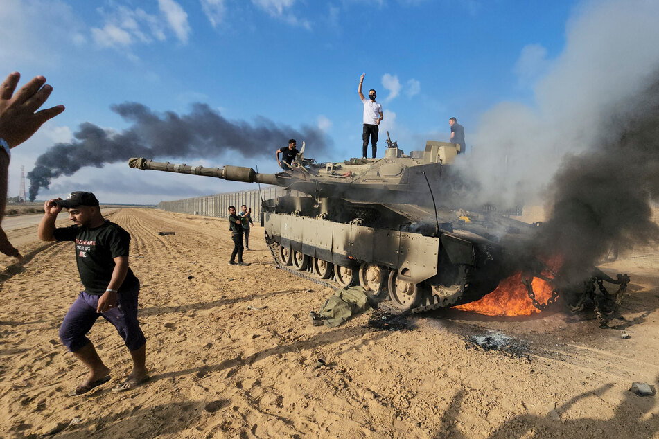 Nach dem Angriff der Hamas auf Israel feiern Palästinenser an einem zerstörten israelischen Panzer am Zaun des Gazastreifens östlich von Khan Younis.