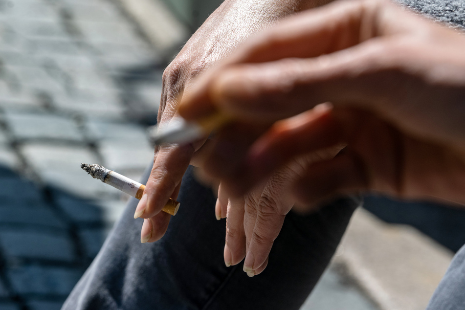 Raucher halten eine brennende Zigarette in der Hand. Die WHO verweist darauf, dass Rauchen das Risiko einer schweren Covid-19-Erkrankung erhöht.