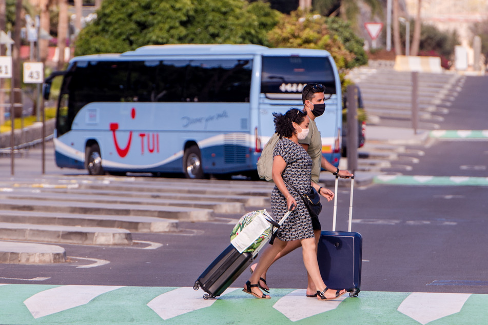 Spanien, Tenerife: Touristen mit Mund-Nasen-Schutz gehen über eine Straße nahe des lokalen Flughafens.